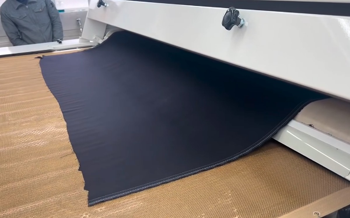 縮絨機（スポンジングマシン）から送り出される紺色の生地。スポンジング加工の様子